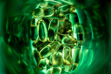 yellow pill capsules spilled out of a green plastic bottle. fish oil. vitamin E. omega-3. on white background