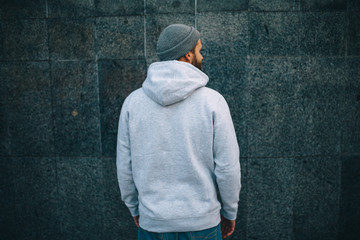 City portrait of handsome hipster guy with beard wearing gray blank hoodie or hoody and hat with...