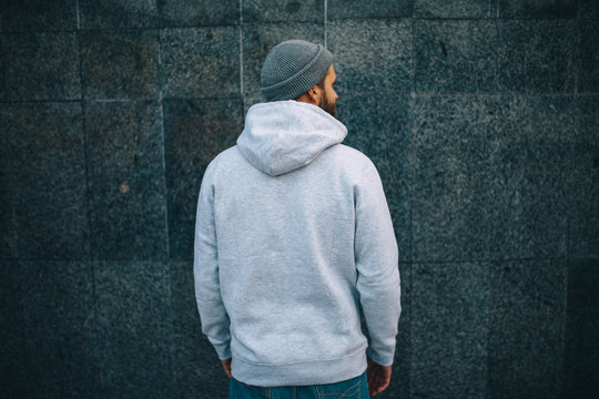 City portrait of handsome hipster guy with beard wearing gray blank hoodie or hoody and hat with space for your logo or design. Mockup for print