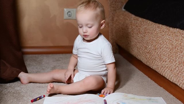 baby girl in a diaper sits on a carpet and draws crayons in an album