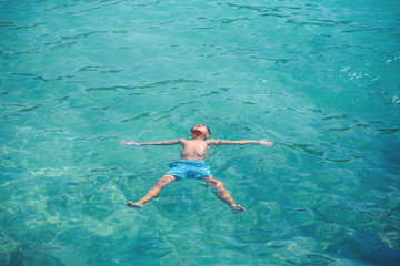 Schoolboy enjoying his summer vacations, he is floating in clear blue water in form of sea star.