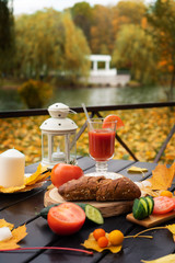 Autumn in the park. Cafe on the street. On the table is tomato juice with ice. Nearby lie cucumbers, tomatoes and rye bread. Autumn still life. Free space for text.