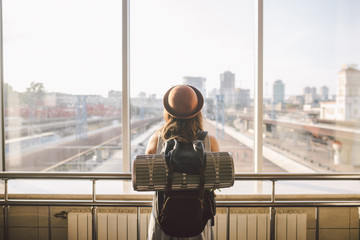 Traveler Rear view woman standing at the window in hall Train Station departure with backpack ,...