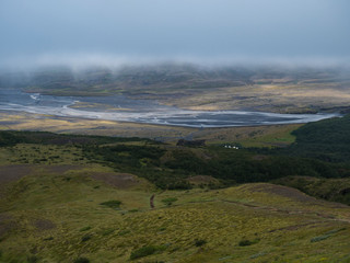 View from top of Valahnukur mountain on landscape of green valley of Thorsmork with volcano huts camp site, sharp green rocks, river Krossa delta and green forest. Foggy summer day, Highlands of