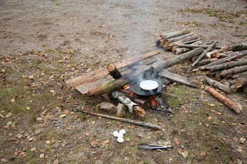 Cooking eggs in a frying pan with water on an adventurous campfire during an outdoor camp in Swedish forests