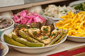 Vegetables fry on a large frying pan on fire. Cooking at the festival. Fried zucchini in a plate on the table.