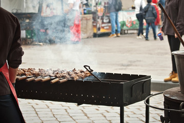 Barbecue fries in the coals. Blurred people eat at the table in the background. Meat and beef at the field kitchen festival.