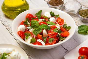 Caprese salad in a bowl on an white wooden table. Selected focus.