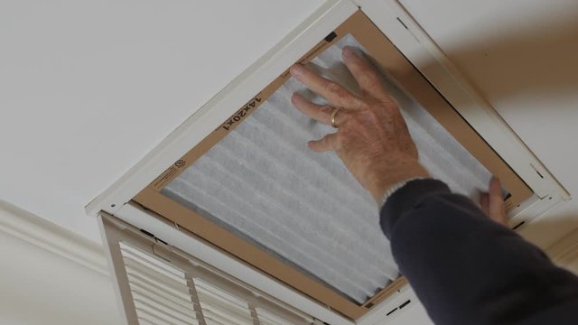 Man replacing dirty HVAC air filter in ceiling vent. Home air duct system maintenance for clean air.