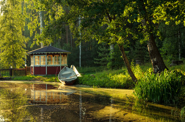 Landscape in a park by the lake during sunset.There is a forest, a gazebo and a boat tied to the...