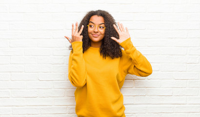 young black woman smiling and looking friendly, showing number nine or ninth with hand forward,...