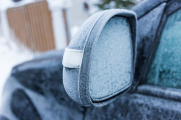 Car's side view mirror of a modern car covered  with snow