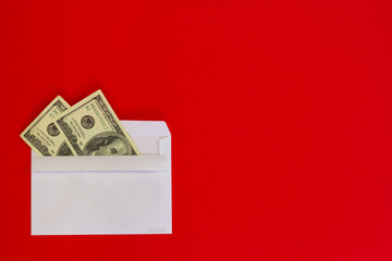  The amount of cash dollars money is cropped with a white envelope for copy space, on a red background. Banknotes folded in an envelope as a present. Sending or saving money, corruption concept