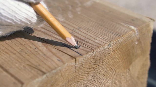 Close up of measurement and marking of a wooden beam with a pencil. Clip. Carpenter in white gloves making marks on wooden bar with pencil and angle ruler, house building process.