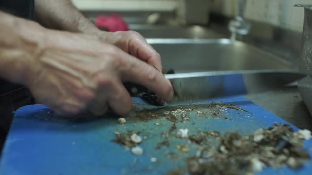 Close up of a cook scrubbing mussels with a chef's knife 