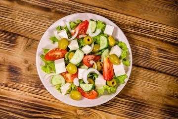 Ceramic plate with greek salad on wooden table. Top view