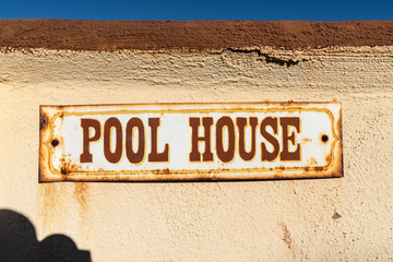 Old rusty pool house sign on stucco wall.  