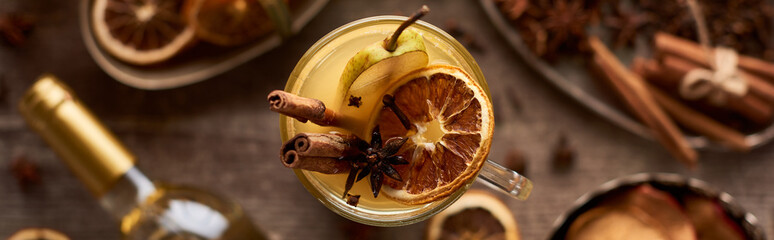 selective focus of pear mulled wine with spices and dried citrus on wooden table, panoramic shot
