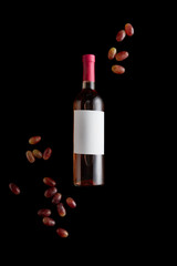 top view of rose wine bottle with blank white label near ripe grape isolated on black