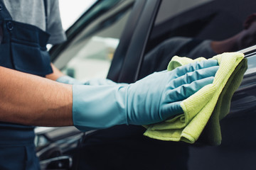 cropped view of car cleaner wiping black car with rag