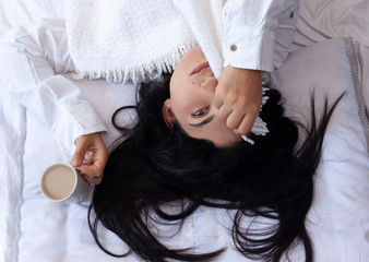 Beauty woman waking up in morning and drinking coffee in bed. Young beautiful woman in bed hiding...