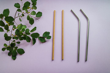 Metallic and bamboo straws with green leaves on pink background. Eco friendly. Sustainable products.