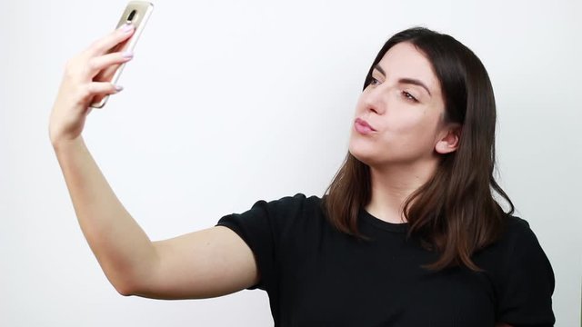 Brown-haired woman makes selfies. Admiring himself in the phone. White background