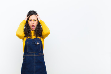 young pretty woman feeling horrified and shocked, raising hands to head and panicking at a mistake...