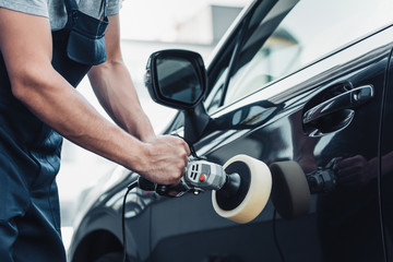 partial view of car cleaner polishing car door with buffer machine