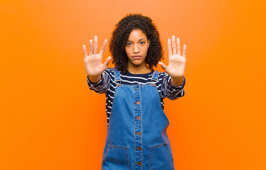 young pretty black woman looking serious, unhappy, angry and displeased forbidding entry or saying...