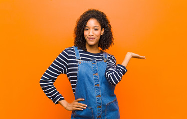 young pretty black woman smiling, feeling confident, successful and happy, showing concept or idea...