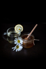 Cup of tea with lemon, camomile and a jar of honey on a black background