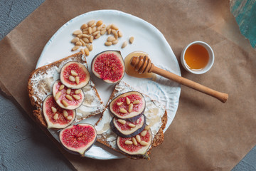 Fig toast with cheese, honey and pine nuts on a white plate. Rustic breakfast or lunch on kraft...