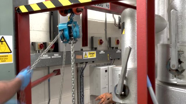 Engineer using a block and tackle in a boiler room to hoist an electric motor