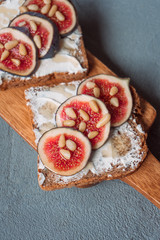 Fig toast with cheese, honey and pine nuts on a wooden board. Rustic breakfast or lunch on a grey...