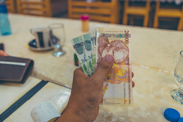 hand holding Armenian Dram banknotes on a table restaurant. Business and finance concept
