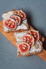 Fig toast with cheese, honey and pine nuts on a wooden board. Rustic breakfast or lunch on a grey...
