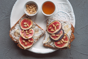 Fig toast with cheese, honey and pine nuts on a white plate. Rustic breakfast or lunch. Pine nuts and honey on a plate top view. 