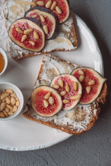Fig toast with cheese, honey and pine nuts on a white plate. Rustic breakfast or lunch. Pine nuts and honey dipper on a plate.