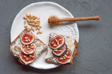 Fig toast with cheese, honey and pine nuts on a white plate. Rustic breakfast or lunch. Pine nuts...