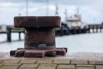 Bollards for mooring ships on the quay wall in a harbor on the German Baltic Sea island of Ruegen. In the background a ship out of focus with beautiful bokeh.