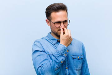 young handsome man feeling disgusted, holding nose to avoid smelling a foul and unpleasant stench