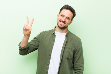 young handsome man smiling and looking friendly, showing number two or second with hand forward,...