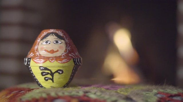 Handmade hand painted Matryoshka Russian doll sitting in front of a fireplace flame fire bokeh still shot
