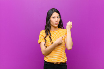 young pretty latin woman looking impatient and angry, pointing at watch, asking for punctuality,...