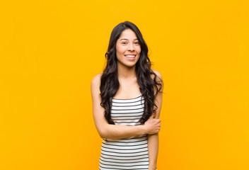 young pretty latin woman laughing shyly and cheerfully, with a friendly and positive but insecure...
