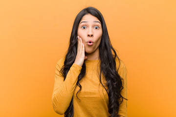young pretty hispanic woman feeling shocked and astonished holding face to hand in disbelief with...