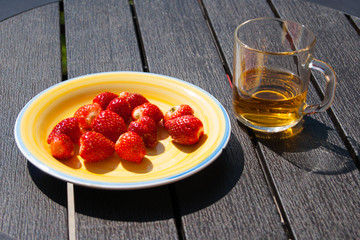 Red berries of garden strawberries with green sepals on a sunny yellow porcelain plate