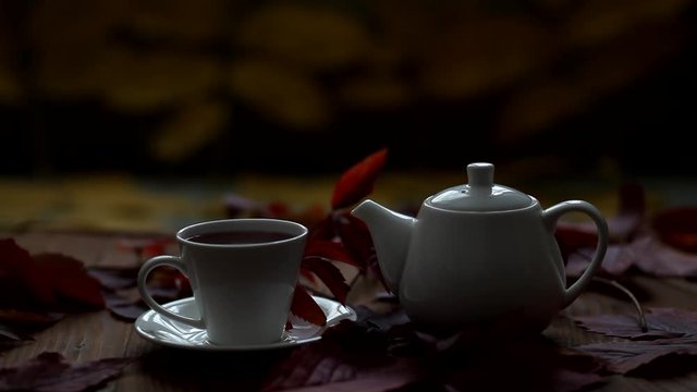 On the table is hot tea and teapot, steam comes from a cup. A drop of tea flows down the teapot spout. Autumn hot drink.