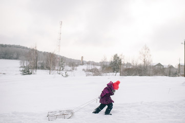 Little child pulling sled up the snowy hill in cold winter day.